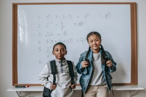 Two kids stand in front of a whiteboard with mathematical equations learning from modern teaching aids