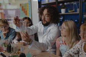 A teacher is doing a lab experiment while kids sit around him learning from modern teaching aids