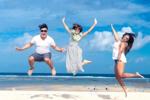 Three people jump up in the air on the beach as they enjoy the sunny Newcastle weather